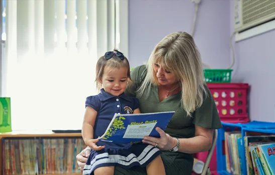 Rainbow Christian Academy teacher with a pre-k student on her lap while she reads her a story